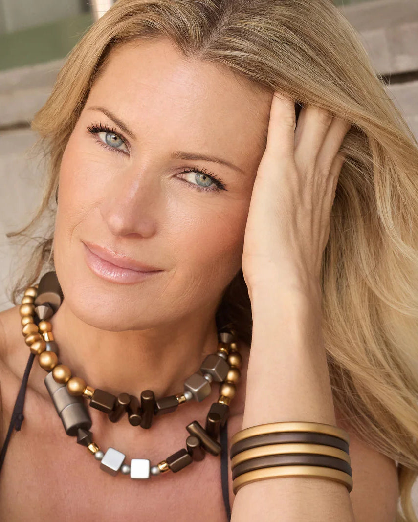 Woman wearing a necklace and bracelets with text 'Light as a Feather... Metallic Magic' on a neutral background