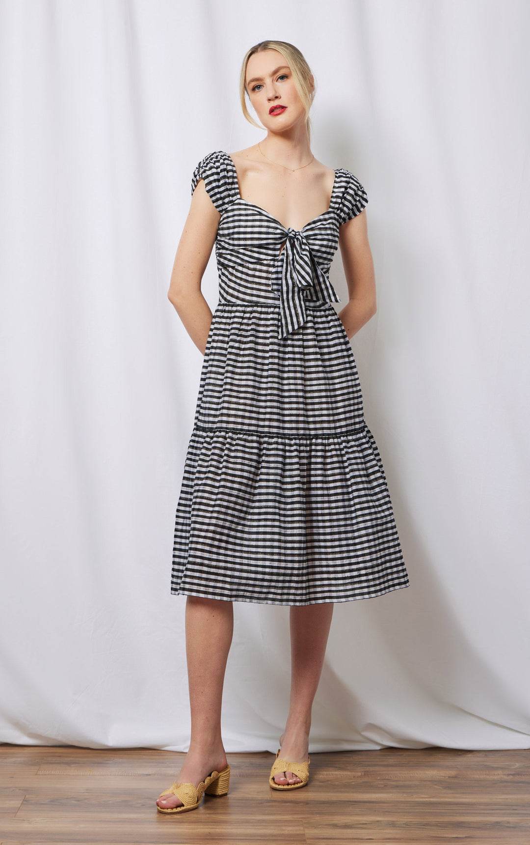 woman with hands behind her wearing black and white cotton and silk blend dress with pockets, front tie detail and rusched shoulder.