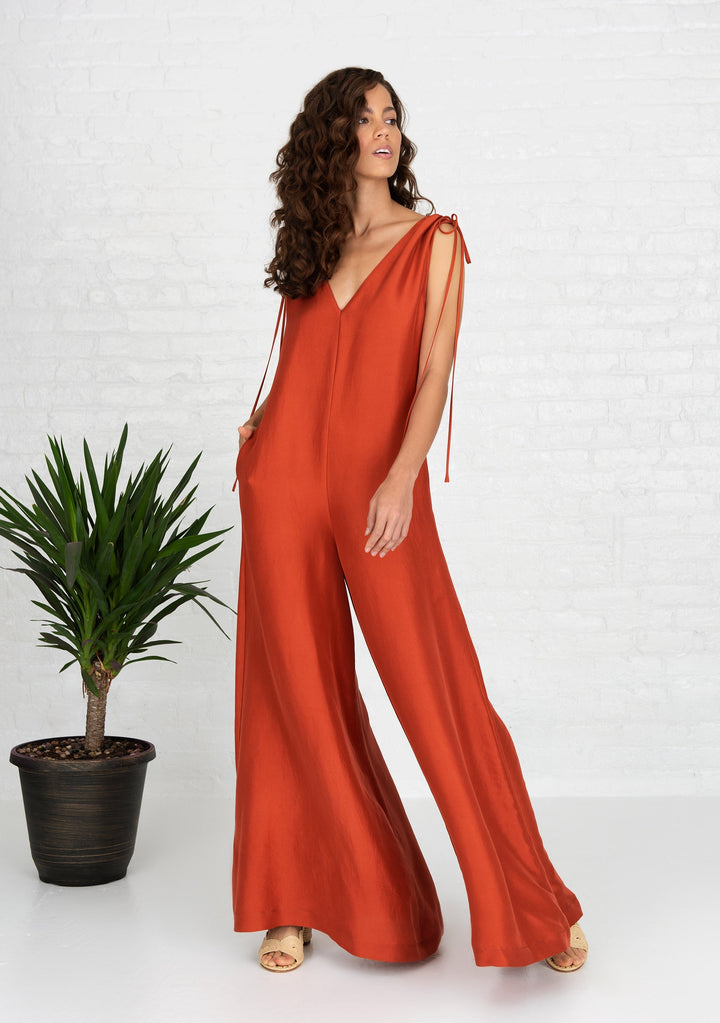 woman wearing burnt orange sleeveless silk jumpsuit with side hand pockets